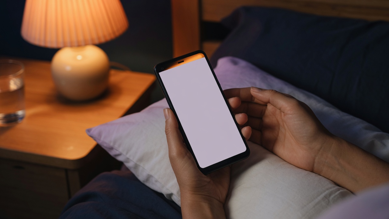 ベッドサイドでスマートフォンを見ながらくつろぐ人の手元